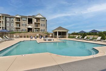 a swimming pool with lounge chairs and umbrellas in front of an apartment building at Aventura at Hawk Ridge, Lake St Louis Missouri